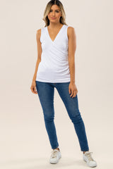 woman wearing a white sleeveless maternity top with a v-neck and ruched detail, paired with blue skinny jeans