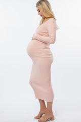 woman wearing a light pink ribbed maternity dress, showing her baby bump in a side profile pose
