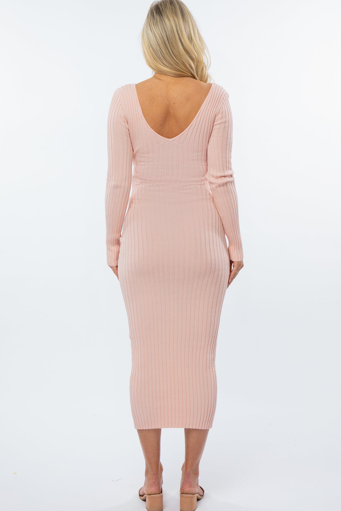 woman wearing a soft pink ribbed maternity dress with a deep v-back and long sleeves, fitted silhouette