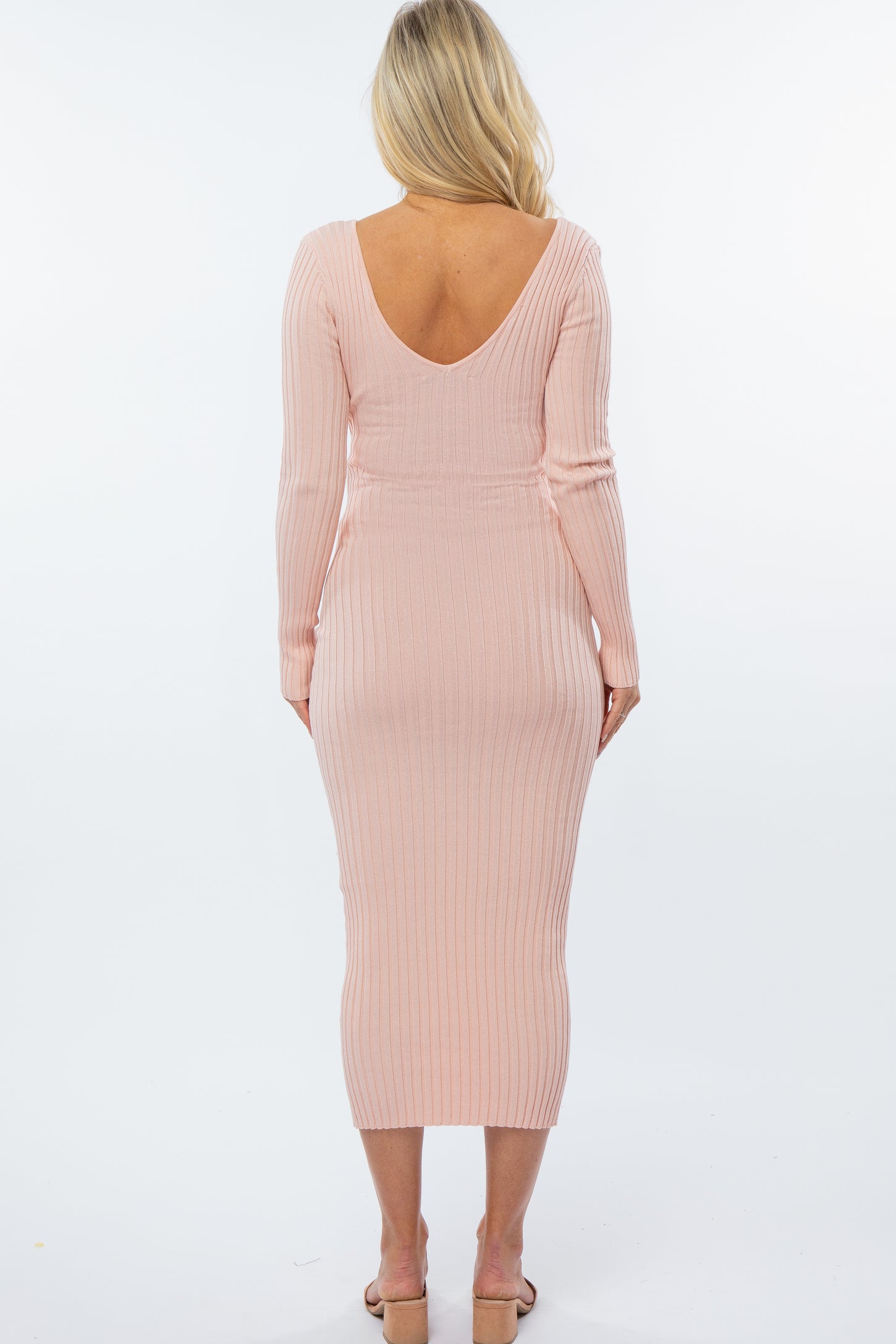 woman wearing a soft pink ribbed maternity dress with a deep v-back and long sleeves, fitted silhouette