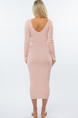 woman wearing a soft pink ribbed maternity dress with a deep v-back and long sleeves, fitted silhouette