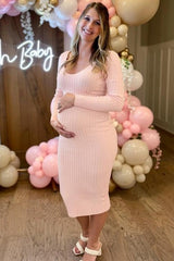 woman wearing a light pink ribbed maternity dress and holding her baby bump