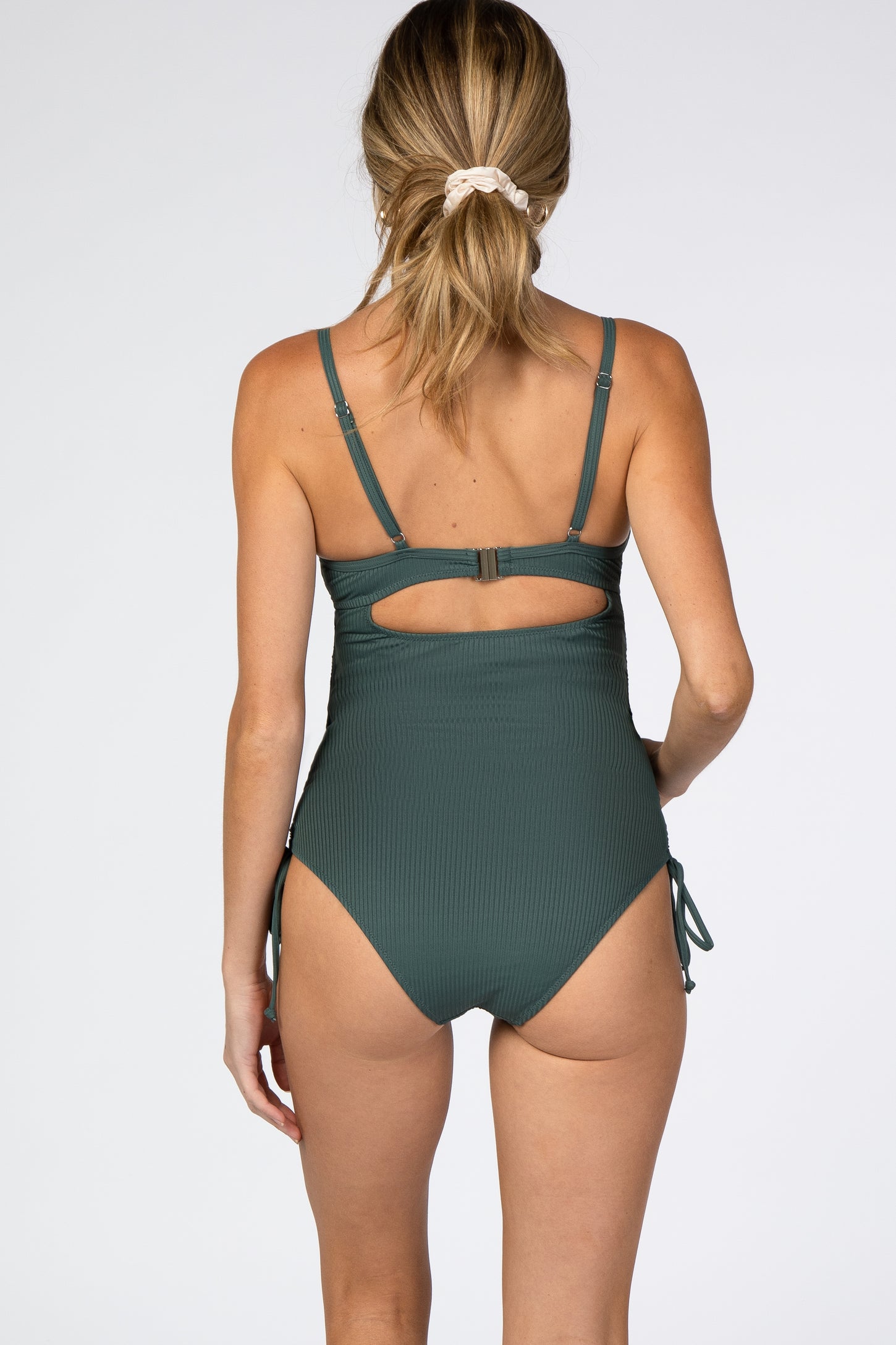 woman wearing a dark green maternity swimsuit with adjustable straps and side ties, showing the back view