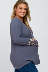 Smiling pregnant woman wearing a blue waffle knit maternity top with leopard print cuffs and blue jeans