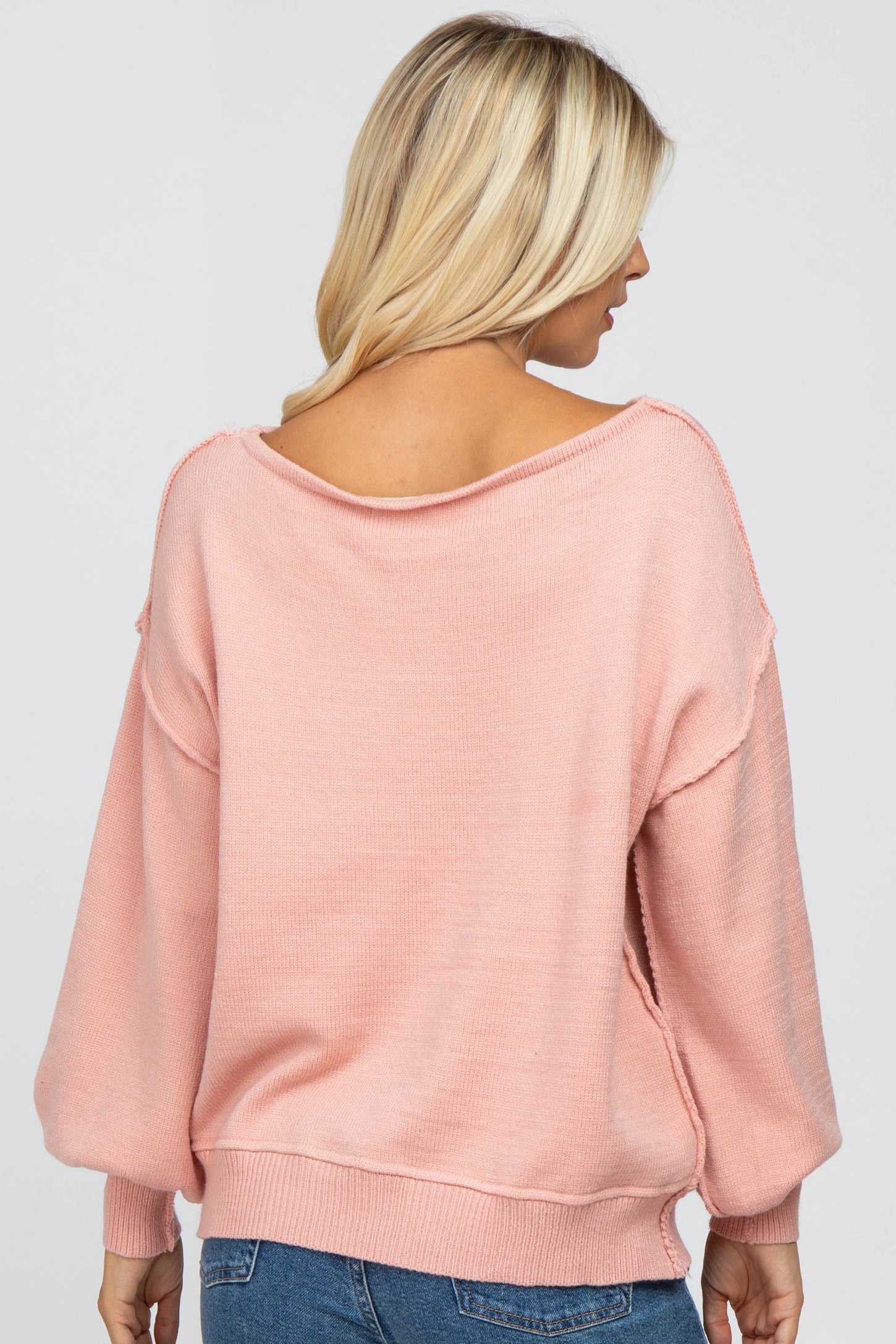 woman wearing a light pink oversized sweater with a wide neckline and side slits, viewed from the back