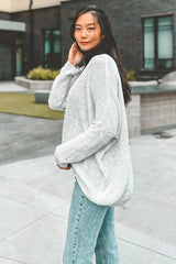 woman wearing a light grey oversized knit sweater and blue high-waisted jeans, posing outside