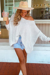 woman wearing an oversized white knit sweater, distressed denim shorts, and a wide-brim hat while holding iced coffee