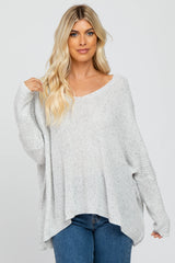 woman wearing a light grey oversized knit sweater with a wide neckline and relaxed fit, paired with blue jeans