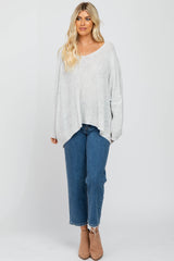 woman wearing a light grey oversized sweater with a scoop neckline and blue high-waisted jeans, paired with ankle boots