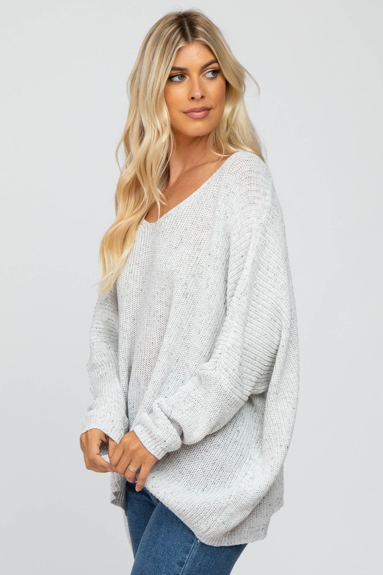 woman wearing a light gray oversized sweater with a v-neck and loose fit, paired with blue jeans