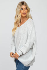woman wearing a light gray oversized sweater with a v-neck and loose fit, paired with blue jeans