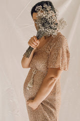 woman wearing a rose gold sequined maternity dress holding a bouquet and showcasing her baby bump