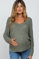woman wearing a sage green knitted maternity sweater and gently cradling her baby bump