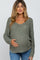 woman wearing a sage green knitted maternity sweater and gently cradling her baby bump
