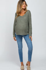 woman wearing a green maternity knit sweater and light blue skinny jeans, showing her baby bump