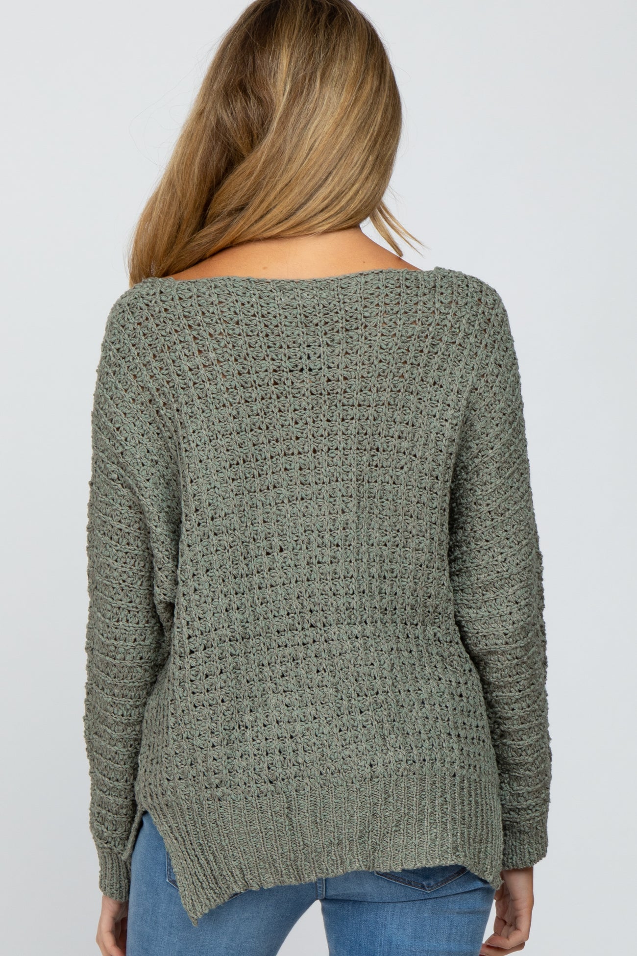 woman wearing a green open knit maternity sweater, viewed from the back, paired with blue jeans