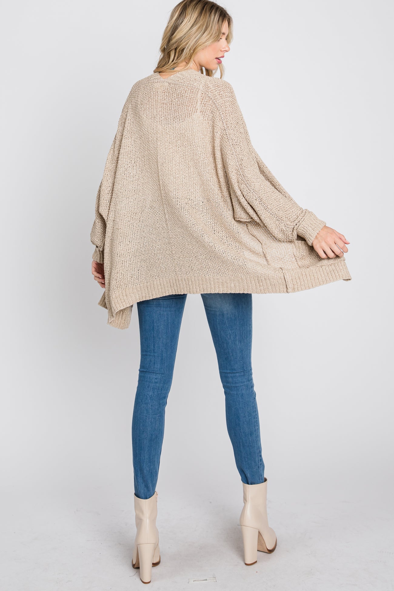 woman wearing a beige oversized knitted sweater paired with blue skinny jeans and beige heeled booties, seen from the back