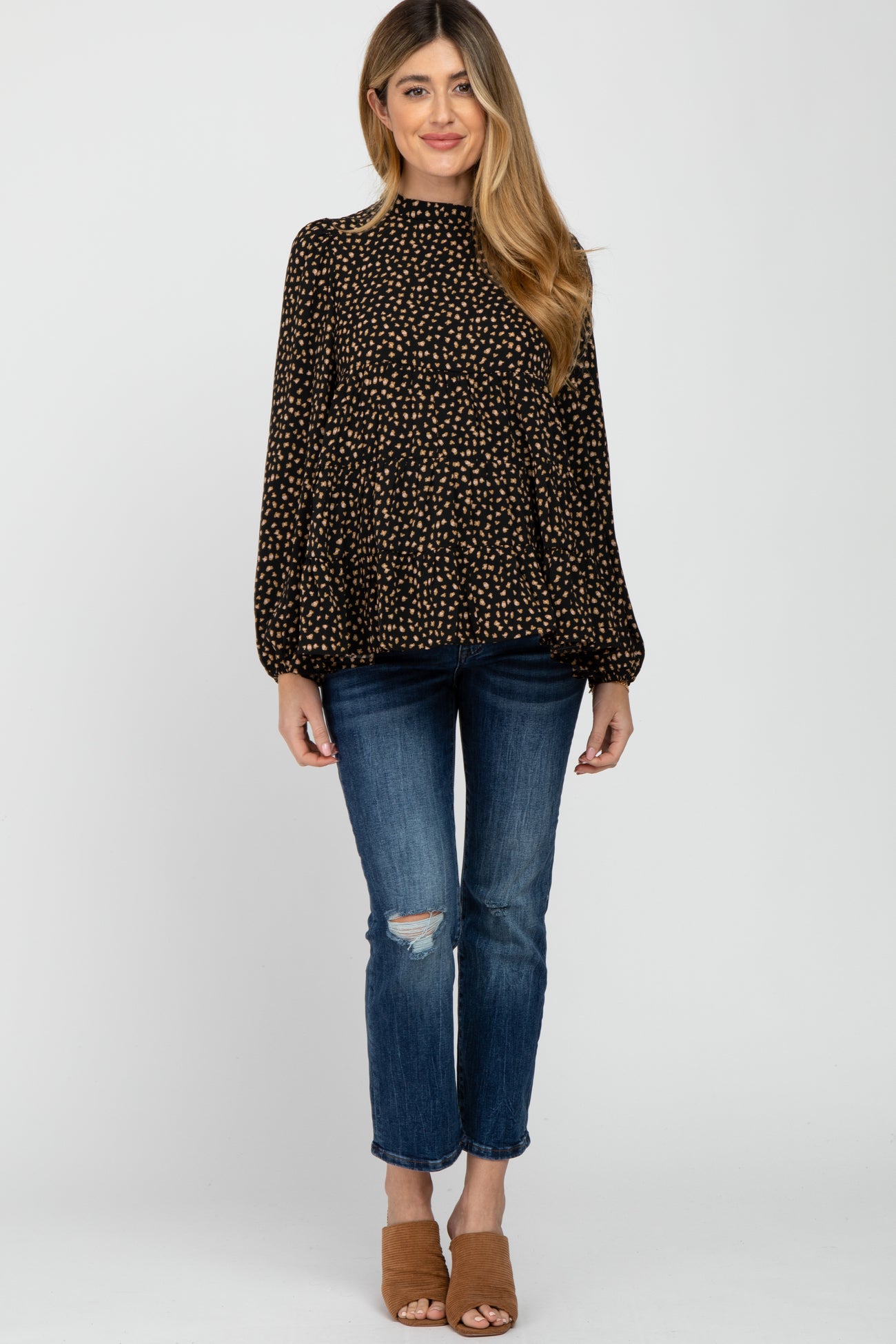woman wearing black and tan leopard print mock neck blouse with distressed blue jeans and brown mules