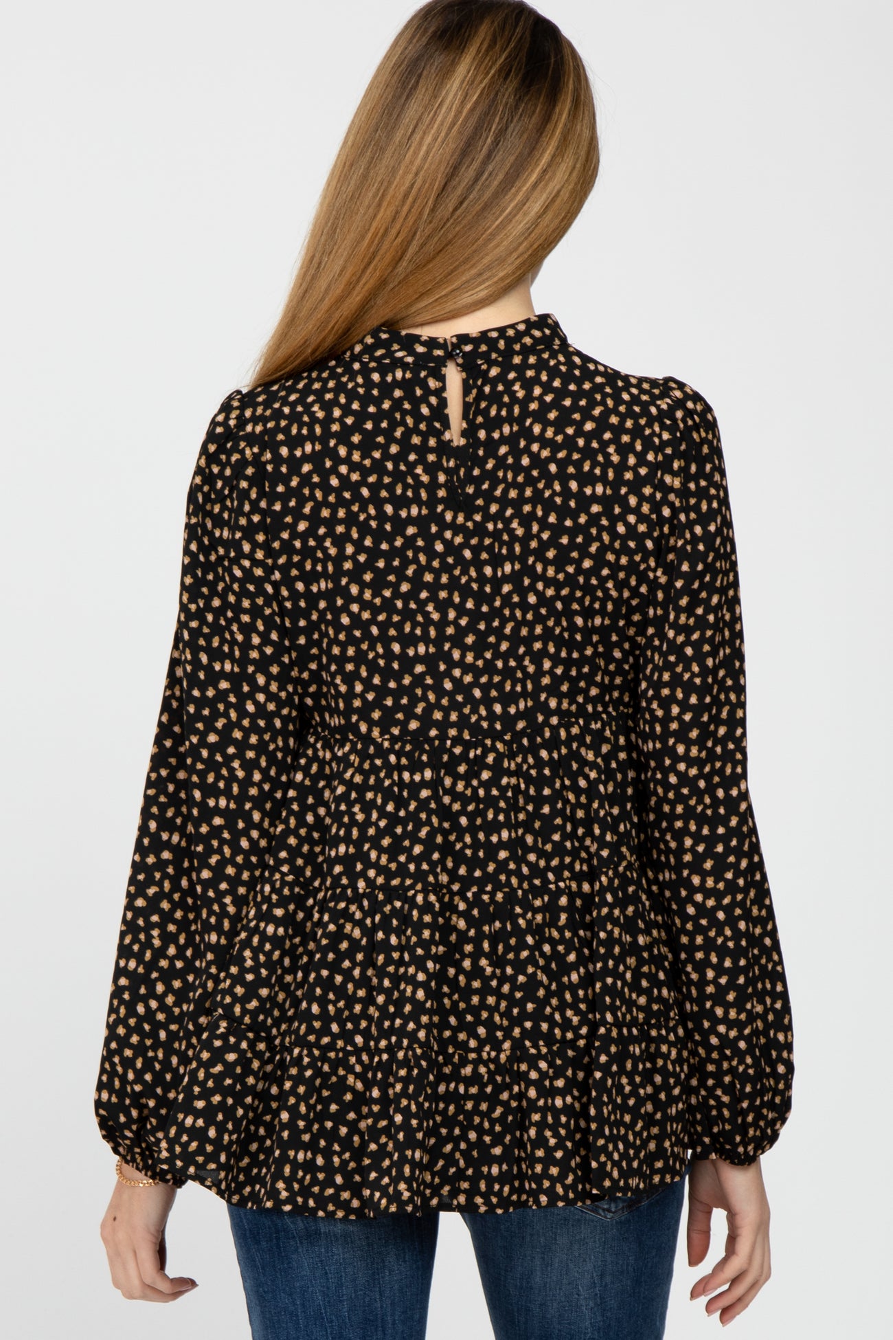 back view of woman wearing black and tan leopard print tiered long sleeve top with high neckline