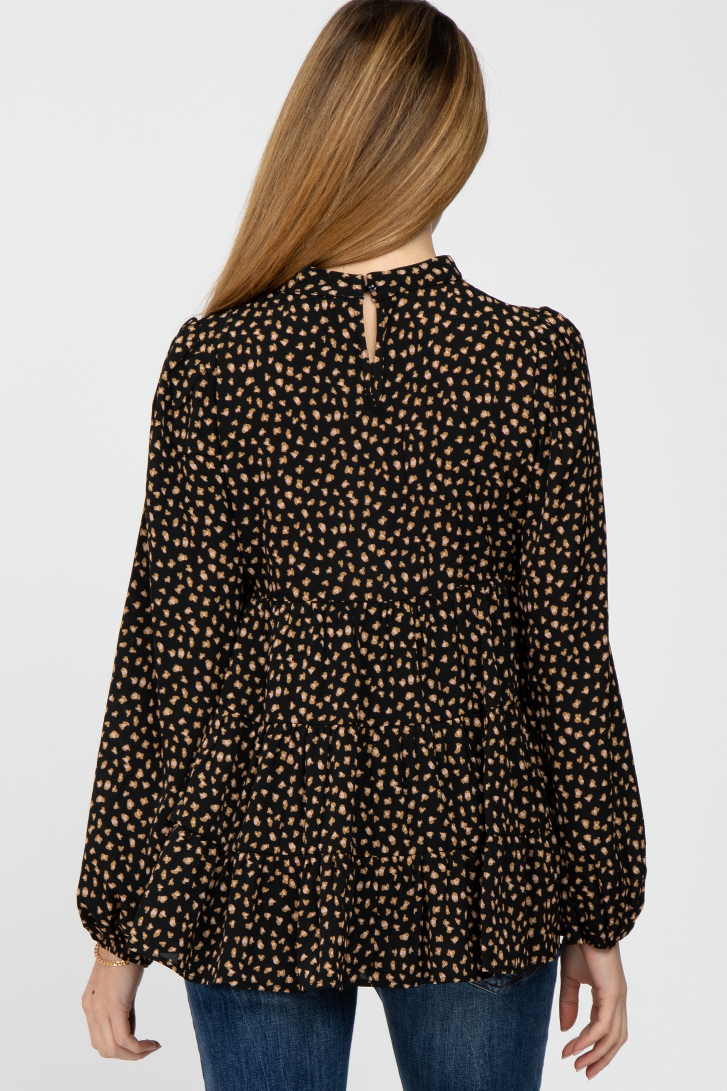 back view of woman wearing black and tan leopard print tiered long sleeve top with high neckline