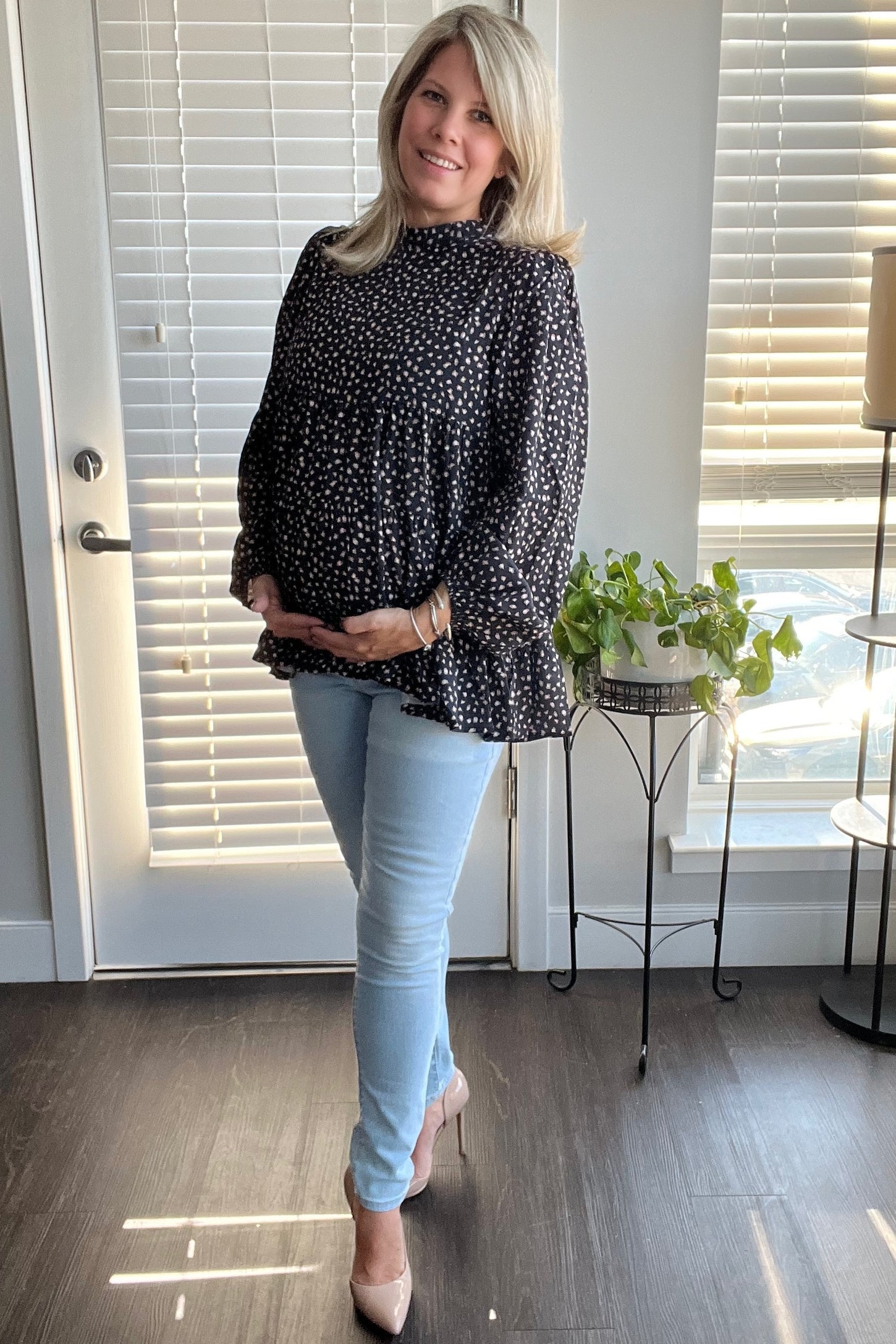 woman wearing a black polka dot maternity top and light blue skinny jeans, showing her baby bump