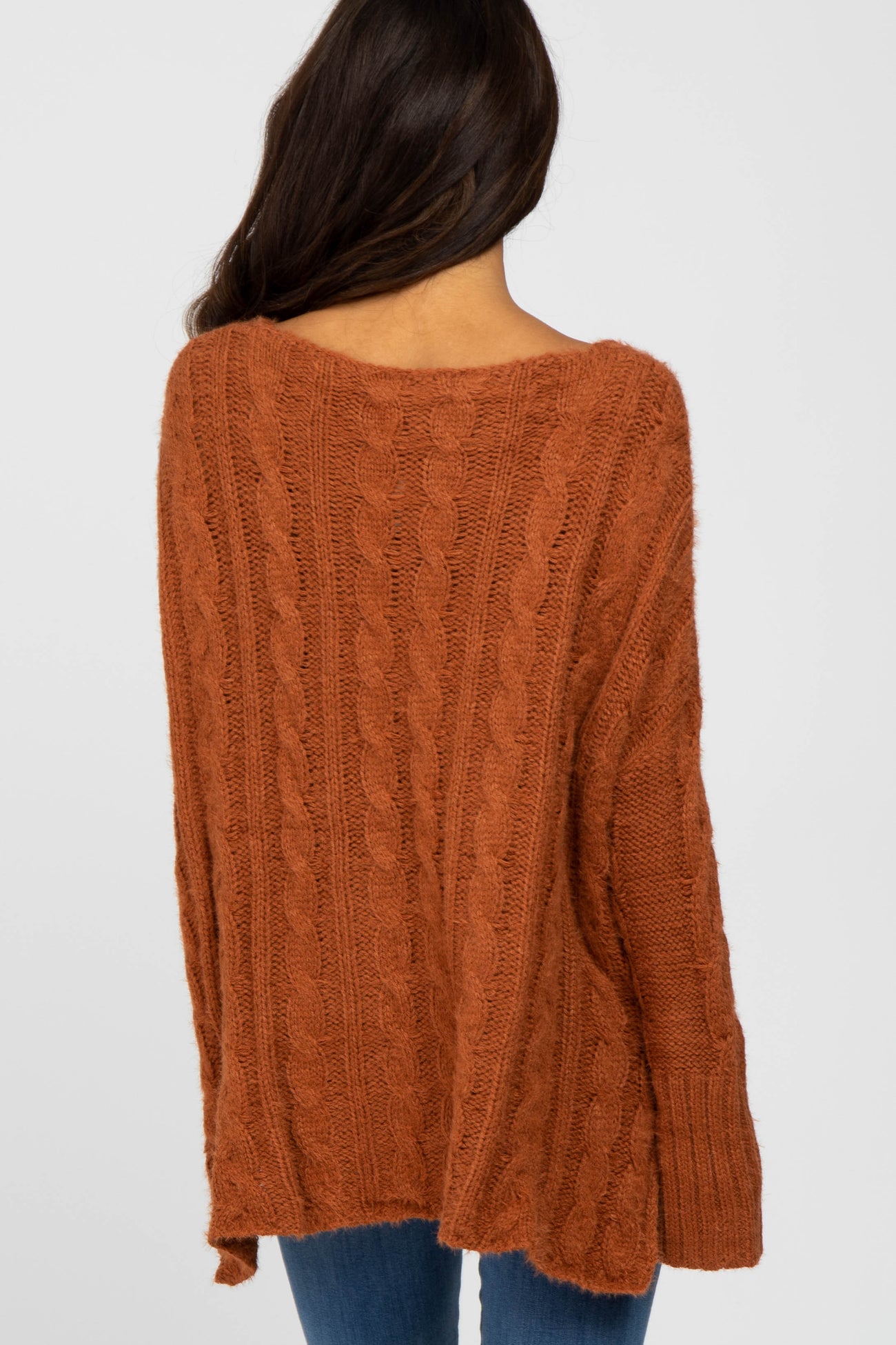 woman wearing an oversized rust cable knit sweater with a relaxed fit and ribbed cuffs, viewed from the back