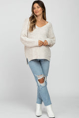 woman wearing a cream knit maternity sweater with a v-neck and side slits paired with distressed jeans and ankle boots