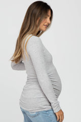 woman wearing a light grey long sleeve maternity top showing her baby bump