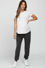 woman wearing a white short sleeve maternity top and gray maternity jogger pants with a baby bump visible