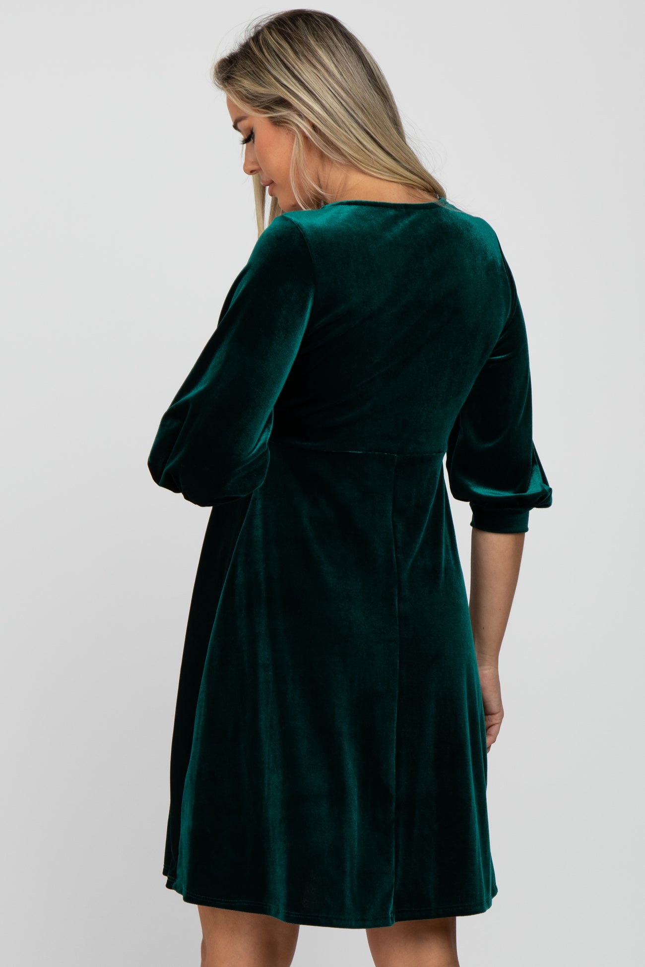 Woman from behind wearing a dark green velvet dress with three-quarter sleeves against a white background