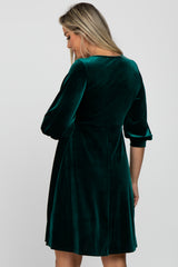 Woman from behind wearing a dark green velvet dress with three-quarter sleeves against a white background