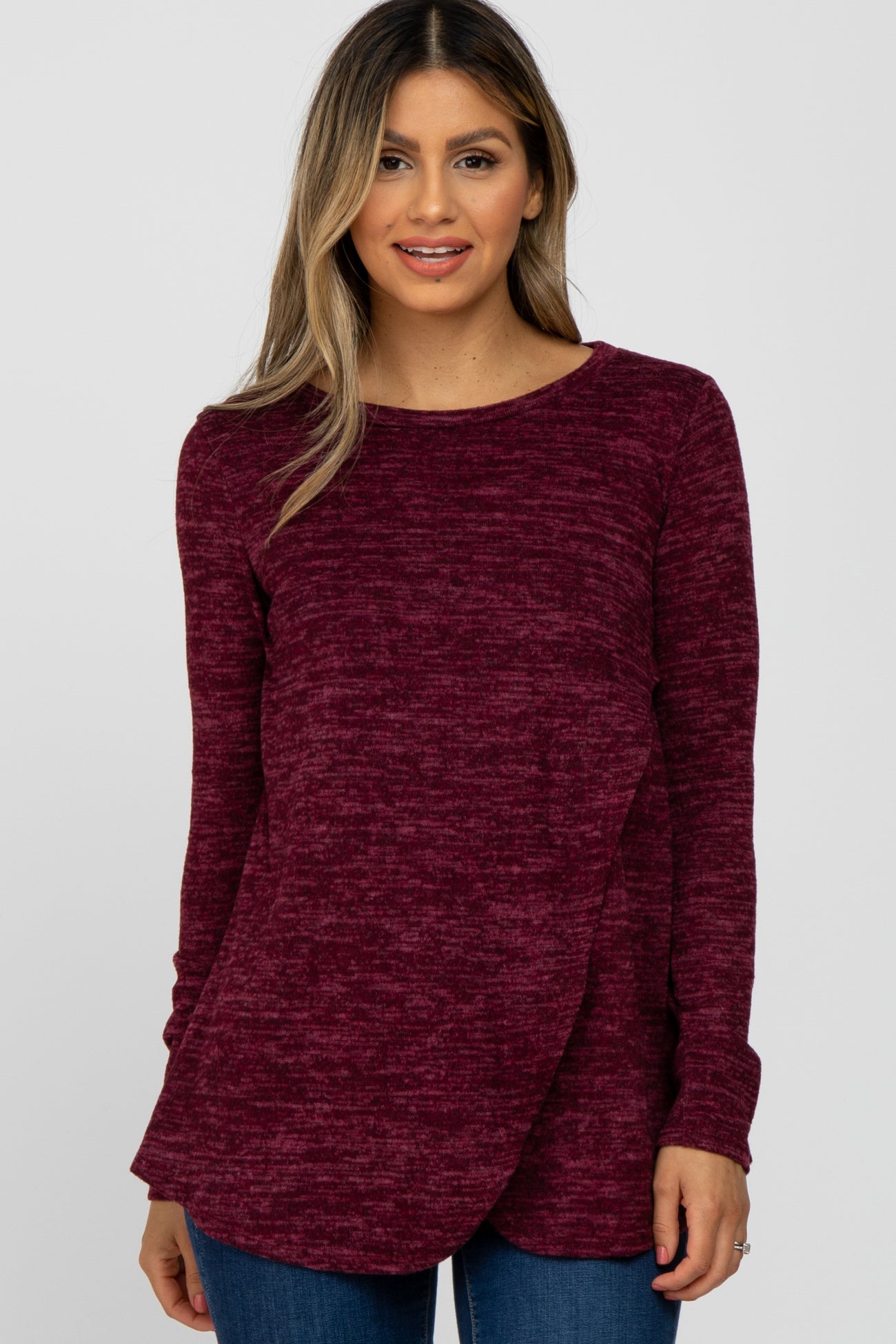 woman wearing a burgundy marled long sleeve top with a crossover front design and relaxed fit, paired with blue jeans