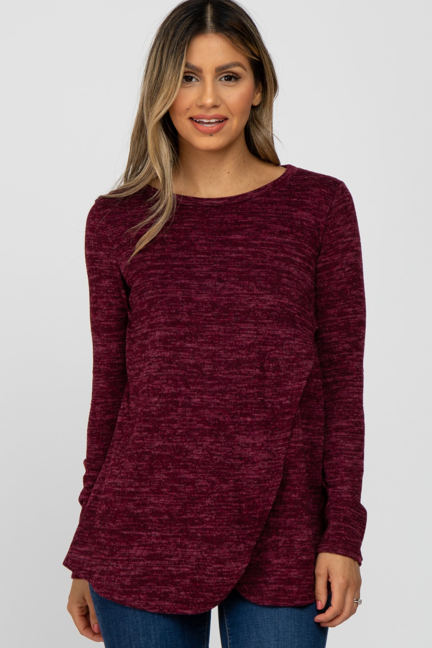 woman wearing a burgundy marled long sleeve top with a crossover front design and relaxed fit, paired with blue jeans