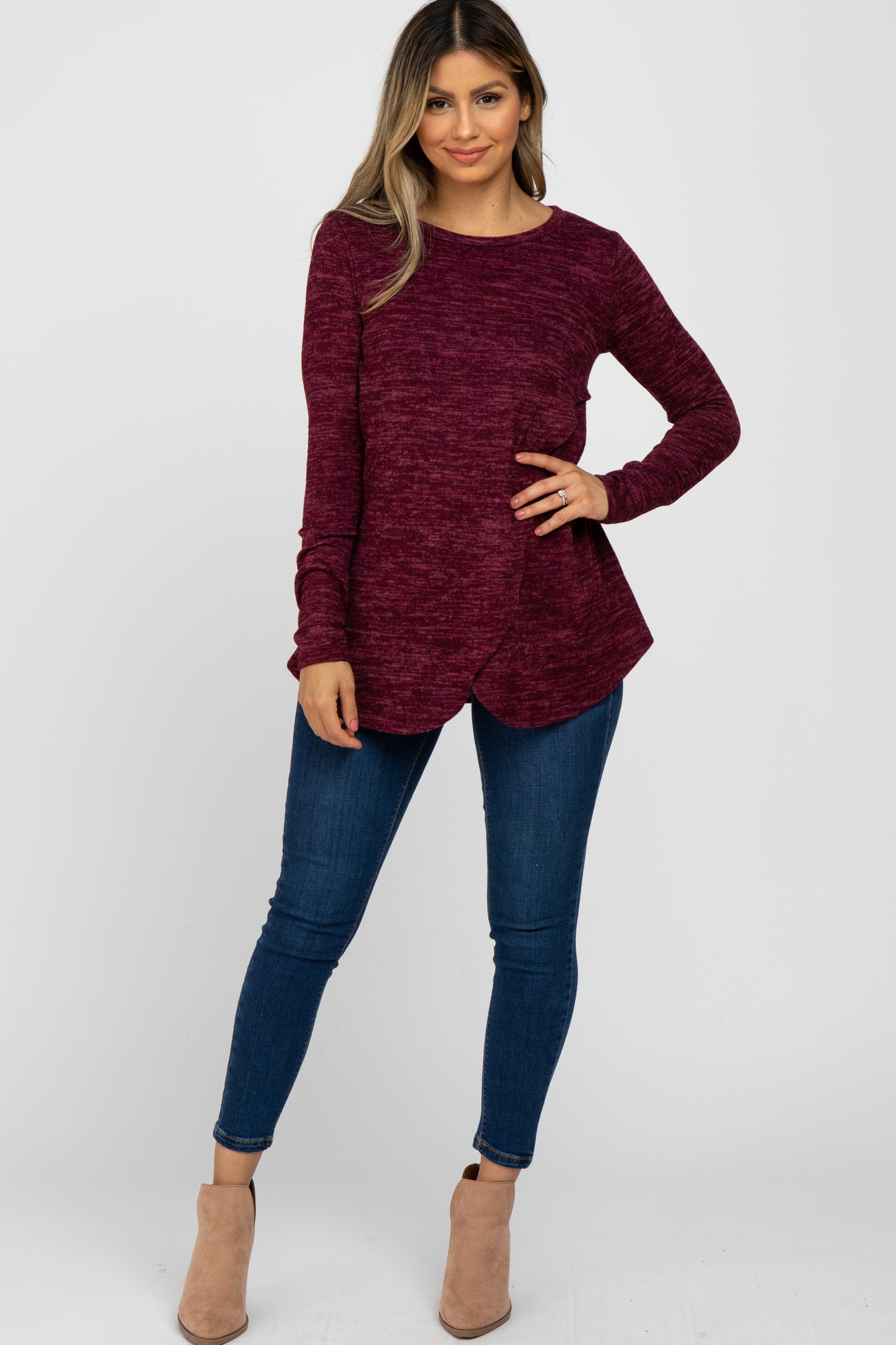 woman wearing a burgundy long sleeve top with a curved hem and blue skinny jeans