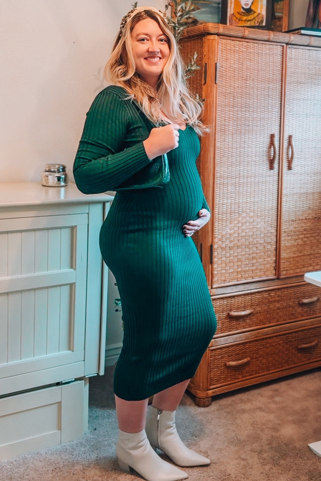 woman wearing a dark green ribbed maternity dress and holding her baby bump, styled with white ankle boots