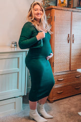 woman wearing a dark green ribbed maternity dress and holding her baby bump, styled with white ankle boots
