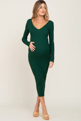woman wearing a dark green ribbed maternity dress with a v-neck and long sleeves, holding her baby bump