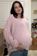 woman wearing a light pink oversized maternity sweater and holding her baby bump