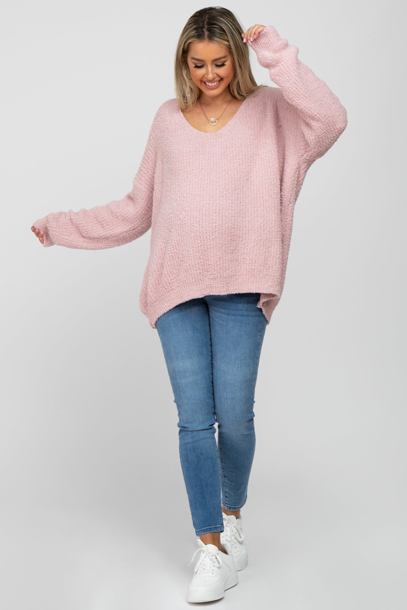 woman wearing a soft pink oversized maternity sweater and blue jeans, with a baby bump visible