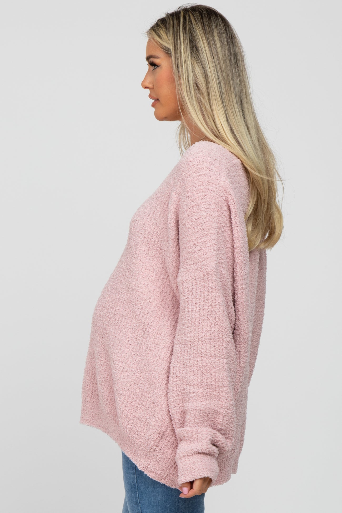 woman wearing a light pink oversized maternity sweater, showcasing her baby bump from the side