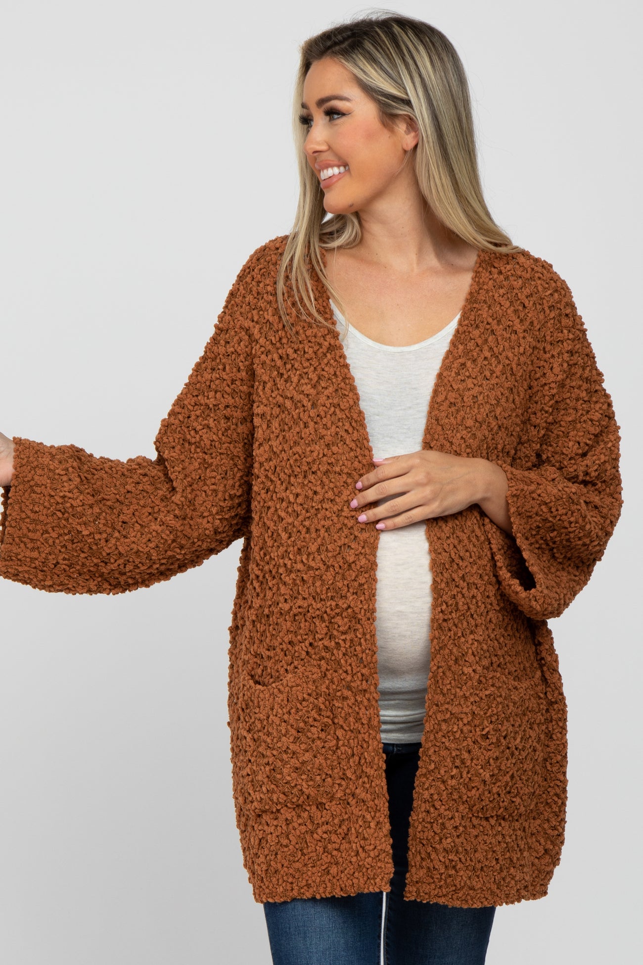 woman wearing a rust-colored maternity cardigan with a textured finish and pockets, showing her baby bump