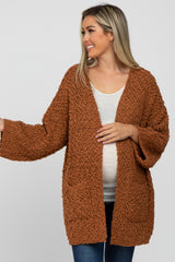 woman wearing a rust-colored maternity cardigan with a textured finish and pockets, showing her baby bump
