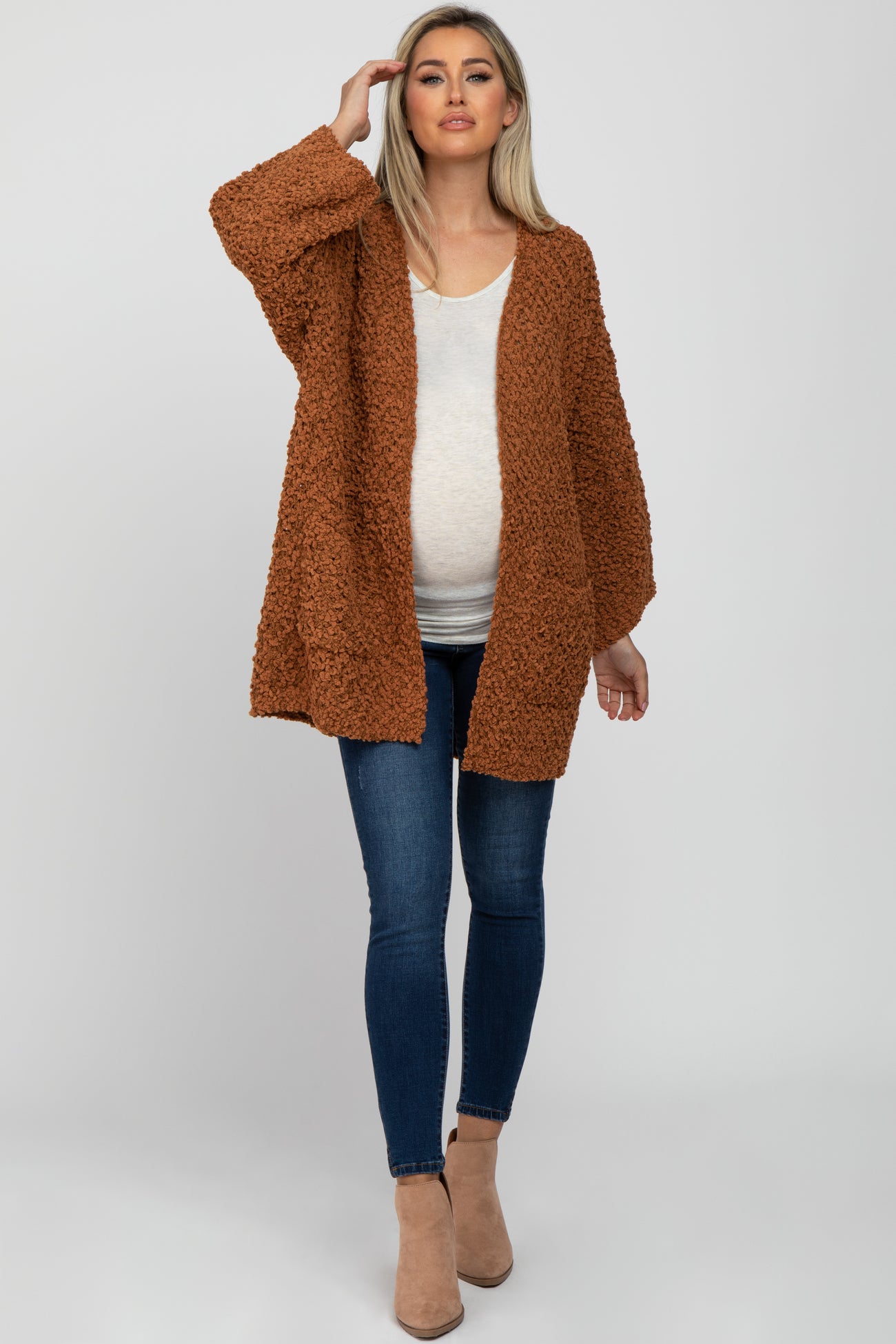 woman wearing a rust-colored oversized maternity cardigan over a white top and blue skinny jeans, showing her baby bump