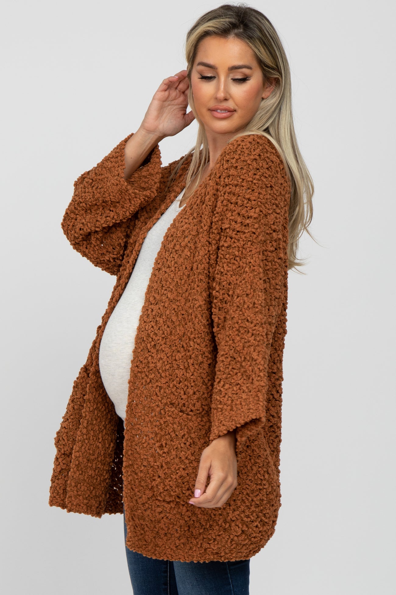 woman wearing a rust-colored knitted maternity cardigan and showing her baby bump