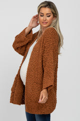 woman wearing a rust-colored knitted maternity cardigan and showing her baby bump