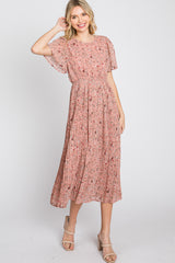 woman wearing a pink floral maxi dress with short sleeves and pleated skirt, posing with one hand in her hair