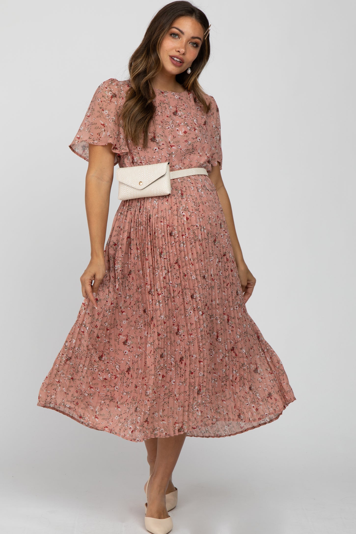 woman wearing a pink floral maternity dress with short sleeves and a pleated skirt, styled with a belt bag