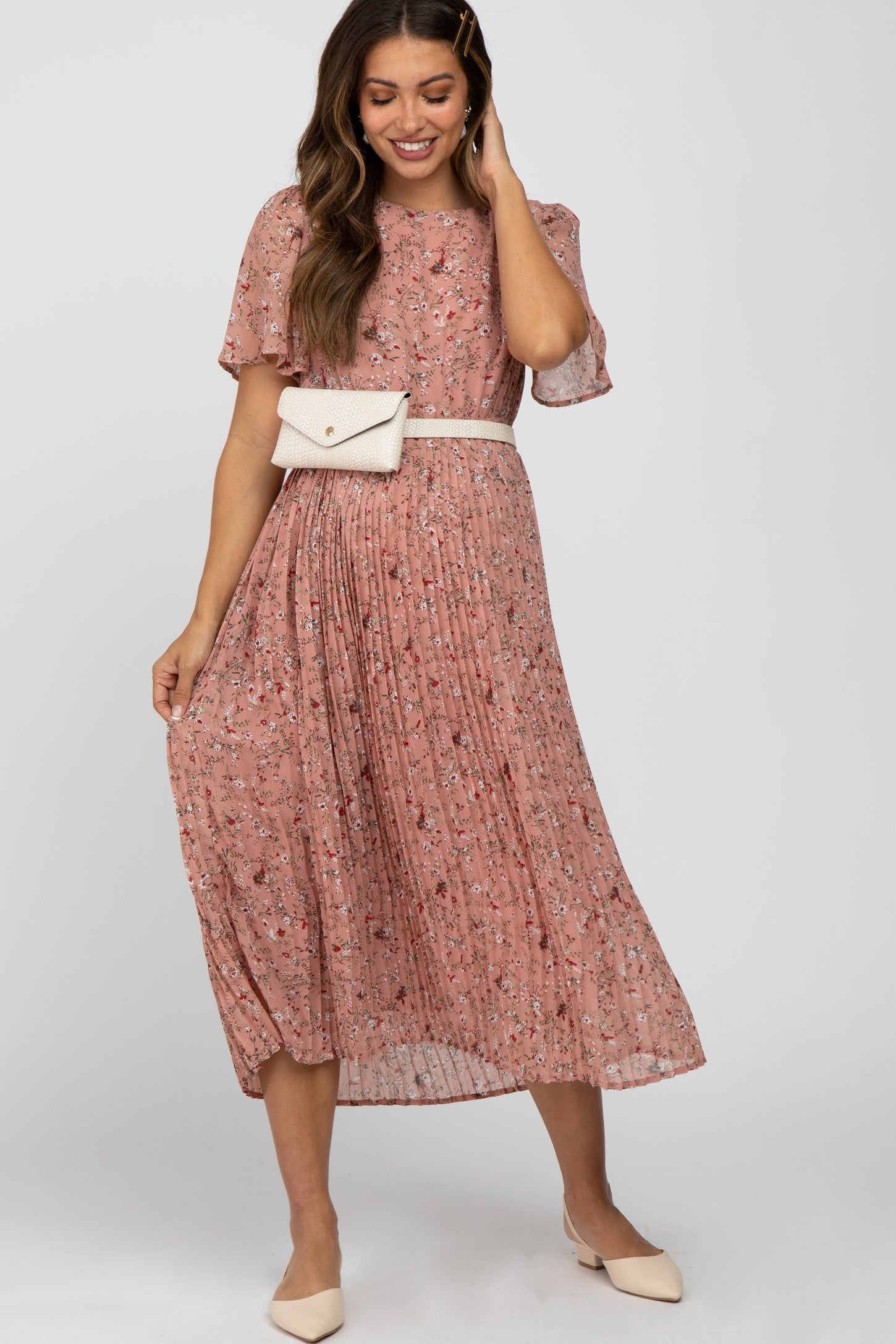 woman wearing a pink floral pleated midi dress with a white belt bag and cream pointed toe flats