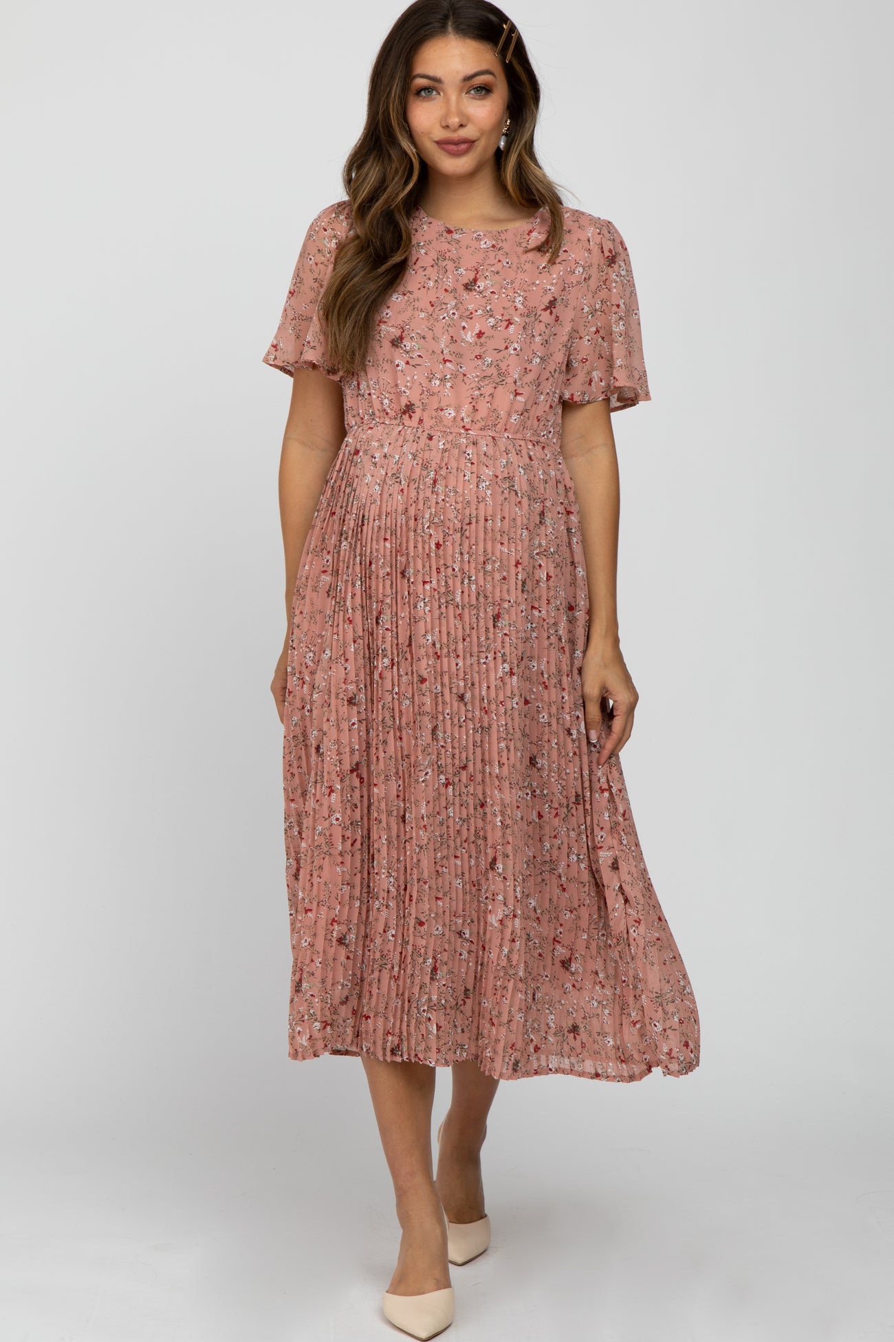 woman wearing a pink floral pleated maternity dress with short sleeves and a flowing silhouette