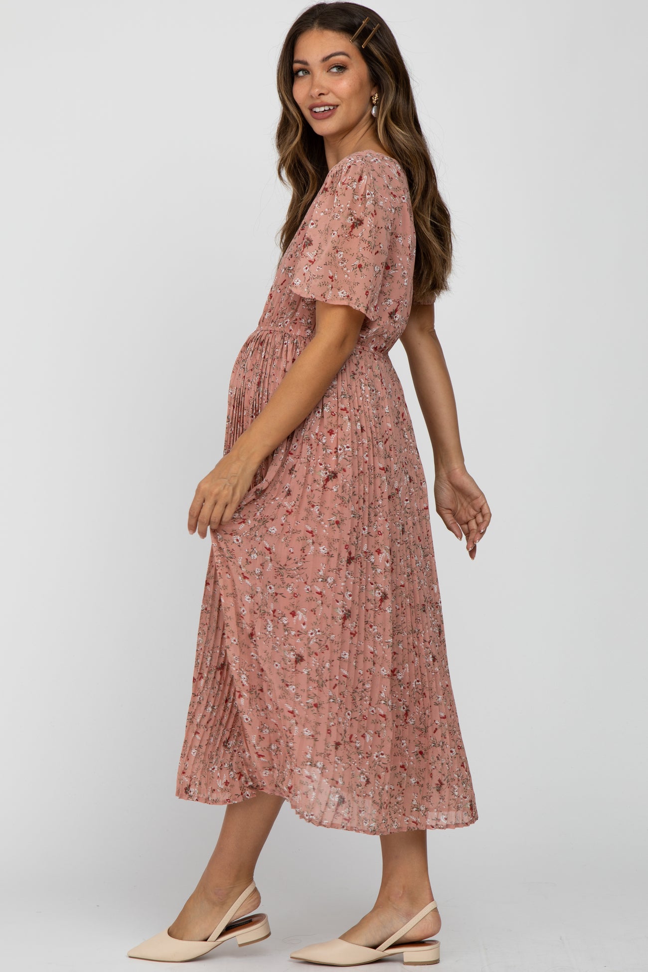 woman wearing a pink floral maternity dress with short sleeves, showing her baby bump and a pleated skirt